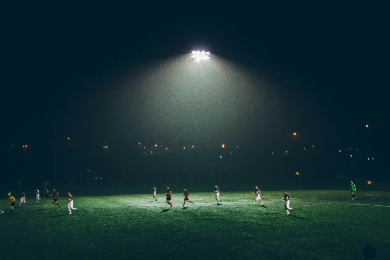 Football players training under floodlights at night — illustration of sports technology and performance comparison on Skuadx.
